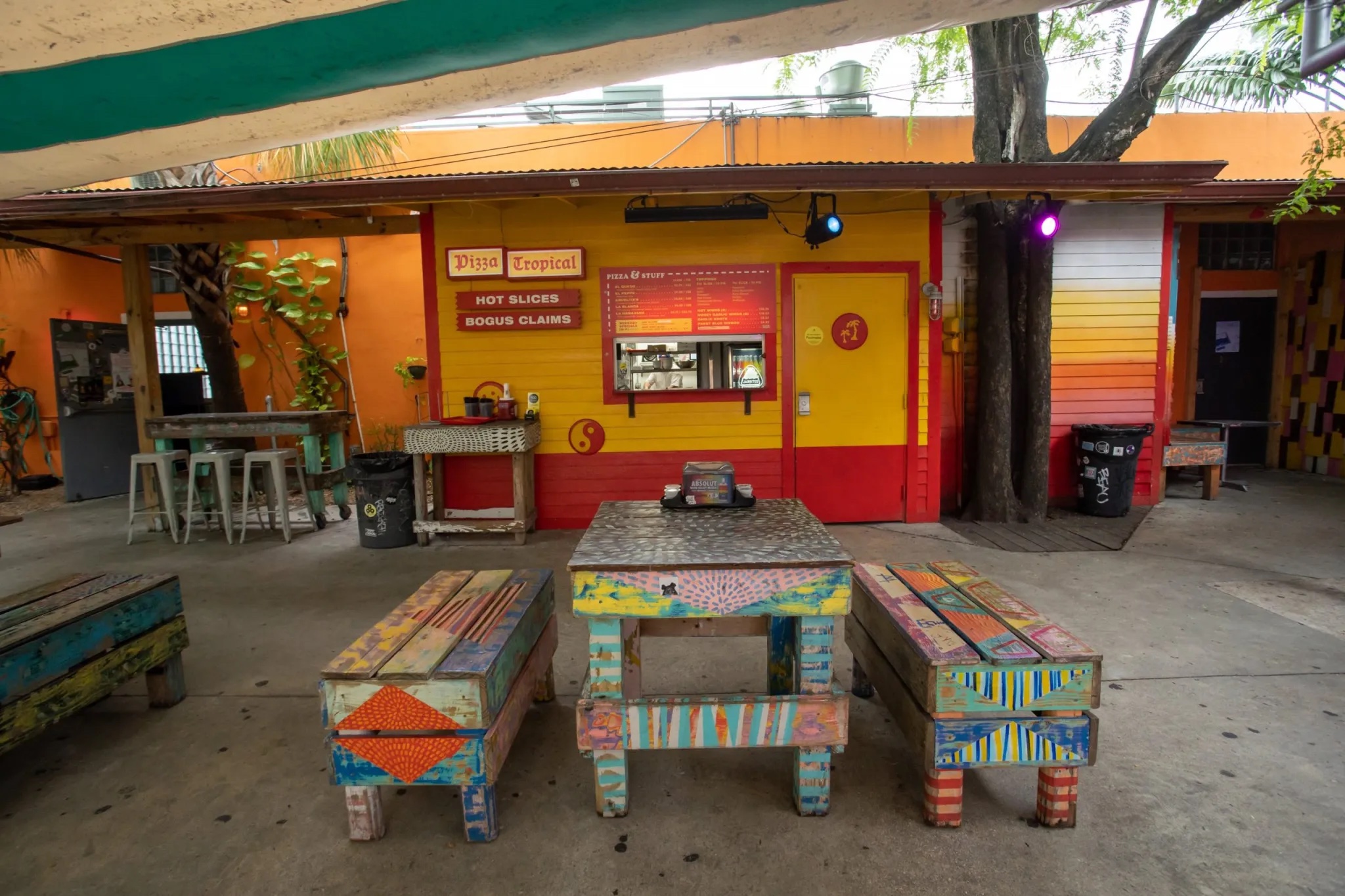 Exterior shot of Pizza Tropical at Gramps restaurant with a consession window and picnic table under a shaded canvas canopy