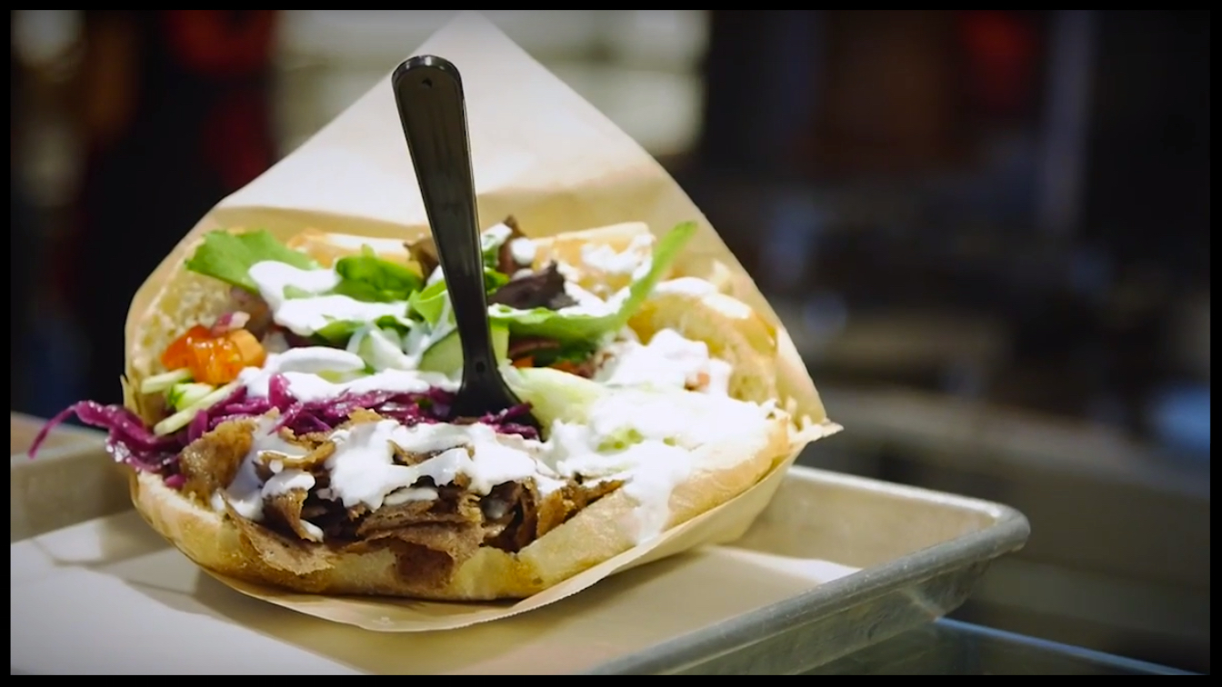 A Doner Kabab with a plastic fork stuck in the middle served on a metal tray 