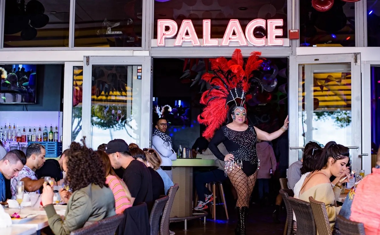 exterior seating area looking inside with people-filled table and a vegas-style showgirl posing in entranceway