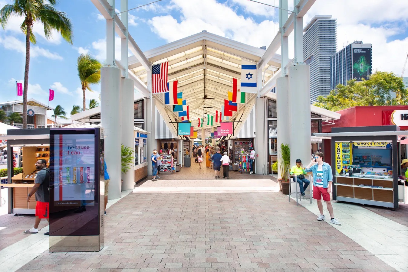 Outside Bayside Marketplace with a pitched roof covering with international flags billowing on the upper beams